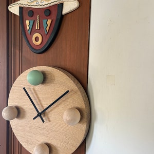 Puede incluir: Un reloj de madera con manecillas negras y cuatro pomos de madera. El reloj est&aacute; montado en una pared de madera marr&oacute;n.
