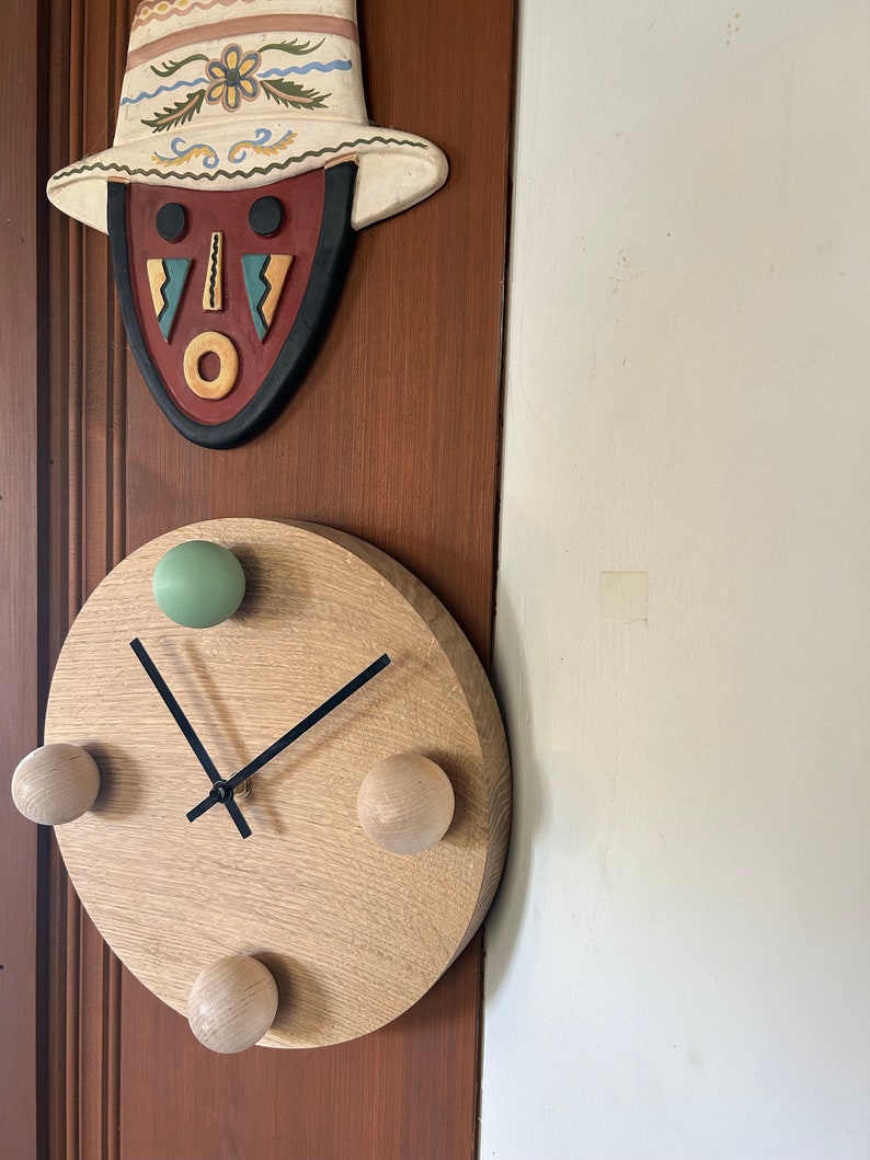 Puede incluir: Un reloj de madera con manecillas negras y cuatro pomos de madera. El reloj est&aacute; montado en una pared de madera marr&oacute;n.