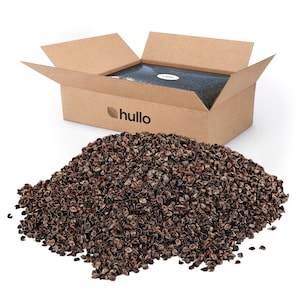 May include: A large pile of dark brown buckwheat hulls sits in front of an open cardboard box. The box is made of brown corrugated cardboard and features the word hullo printed in black text with a small leaf icon to the left of the brand name.