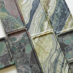 May include: A collection of rectangular stone trays featuring varied natural patterns. Some trays display a dark, speckled granite-like texture in shades of green, black, and brown, while others exhibit smooth, swirling bands of light and dark green marble.