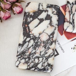 May include: A rectangular slab of polished white marble featuring prominent black veining and subtle pinkish undertones. The stone surface is smooth and glossy, displaying a complex, fractured pattern throughout the entire piece.