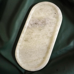 May include: A light green, oval-shaped tray with a polished surface. The tray has a slightly textured appearance with subtle variations in color. A small hole is visible near one end. The tray is set against a dark green background.