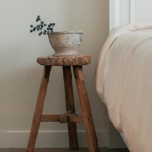 May include: A rustic wooden stool with three legs, painted white, and a white ceramic planter with a sprig of blue berries on top.