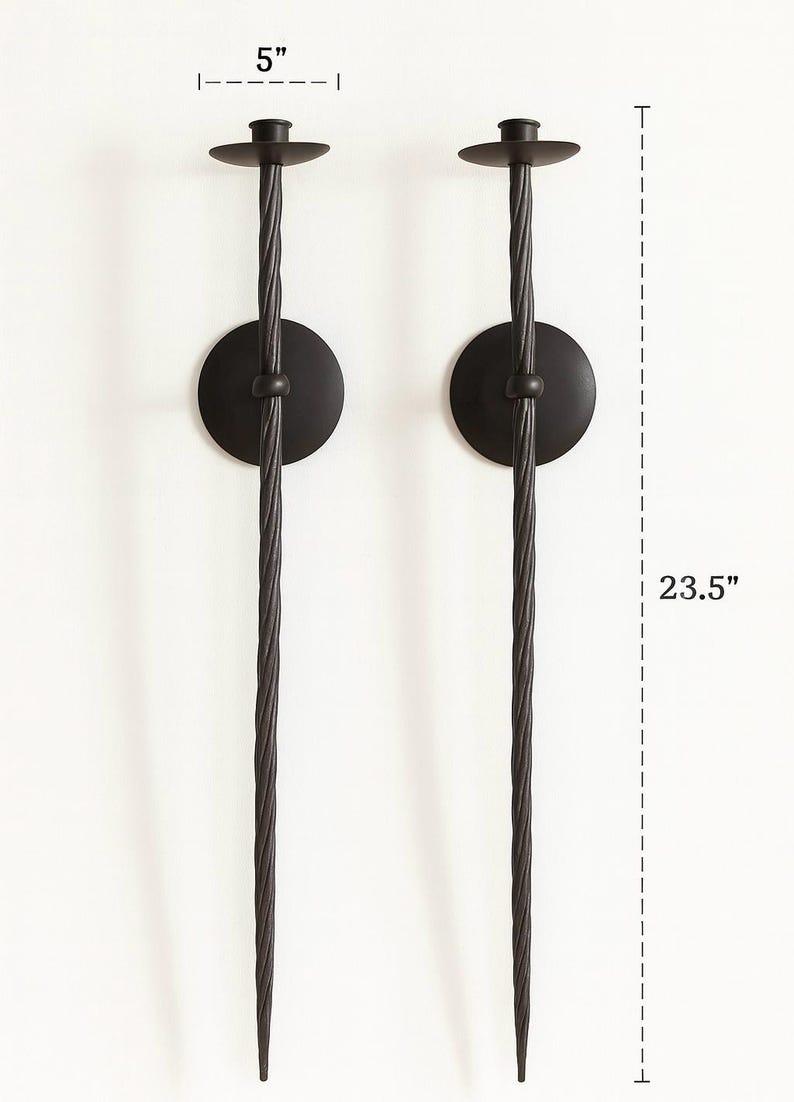 May include: Two black metal wall sconces. Each sconce has a circular base, a twisted stem, and a small, round candle holder. The sconces are 23.5 inches tall and 5 inches wide.