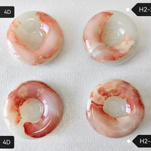 May include: Four circular, translucent white resin objects with swirling coral-pink patterns. Each piece features a central hole and is labeled with black tags reading H2-1: 4D, H2-2: 4D, H2-3: 4D, and H2-4: 4D, identifying each unique item.