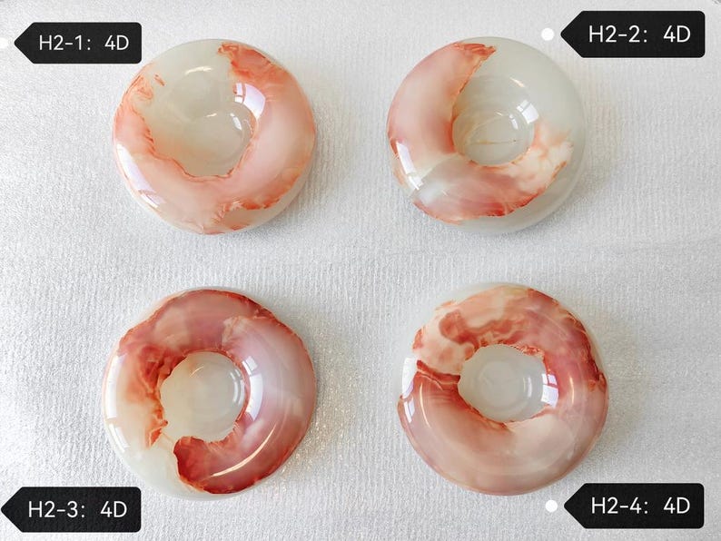 May include: Four circular, translucent white resin objects with swirling coral-pink patterns. Each piece features a central hole and is labeled with black tags reading H2-1: 4D, H2-2: 4D, H2-3: 4D, and H2-4: 4D, identifying each unique item.