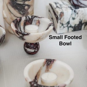 Puede incluir: Un cuenco peque&ntilde;o con pie y un cuenco peque&ntilde;o de m&aacute;rmol blanco con vetas de color morado oscuro y negro. Cada cuenco contiene una peque&ntilde;a vela de t&eacute; blanca. El texto Small Footed Bowl y Small Bowl aparece junto a los objetos.