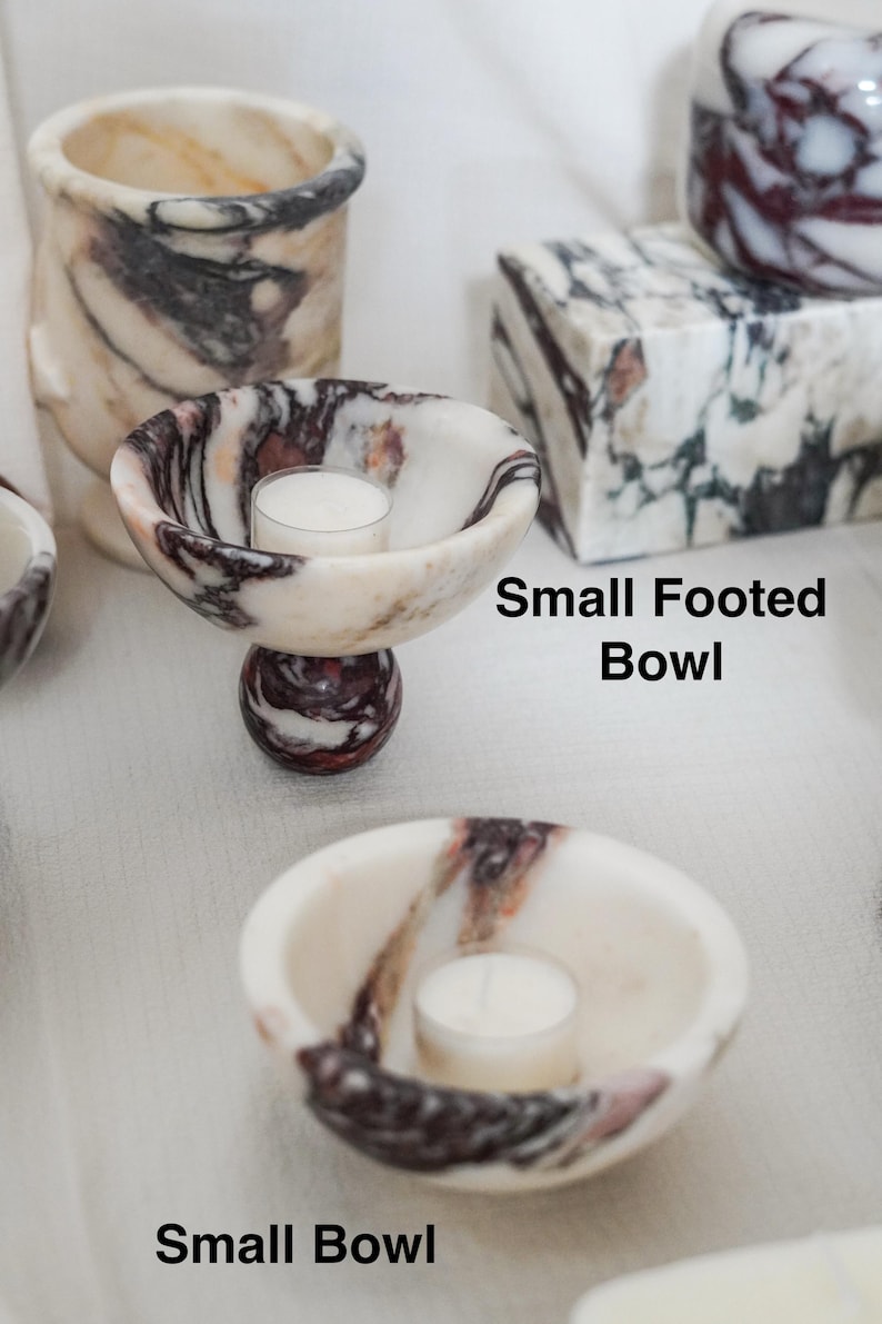 Puede incluir: Un cuenco peque&ntilde;o con pie y un cuenco peque&ntilde;o de m&aacute;rmol blanco con vetas de color morado oscuro y negro. Cada cuenco contiene una peque&ntilde;a vela de t&eacute; blanca. El texto Small Footed Bowl y Small Bowl aparece junto a los objetos.