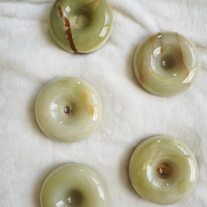 May include: Five circular, donut-shaped stones made of polished green onyx. Each piece features a smooth, glossy surface with natural variations in color, including light green tones and distinct brown mineral veins running through the stone.
