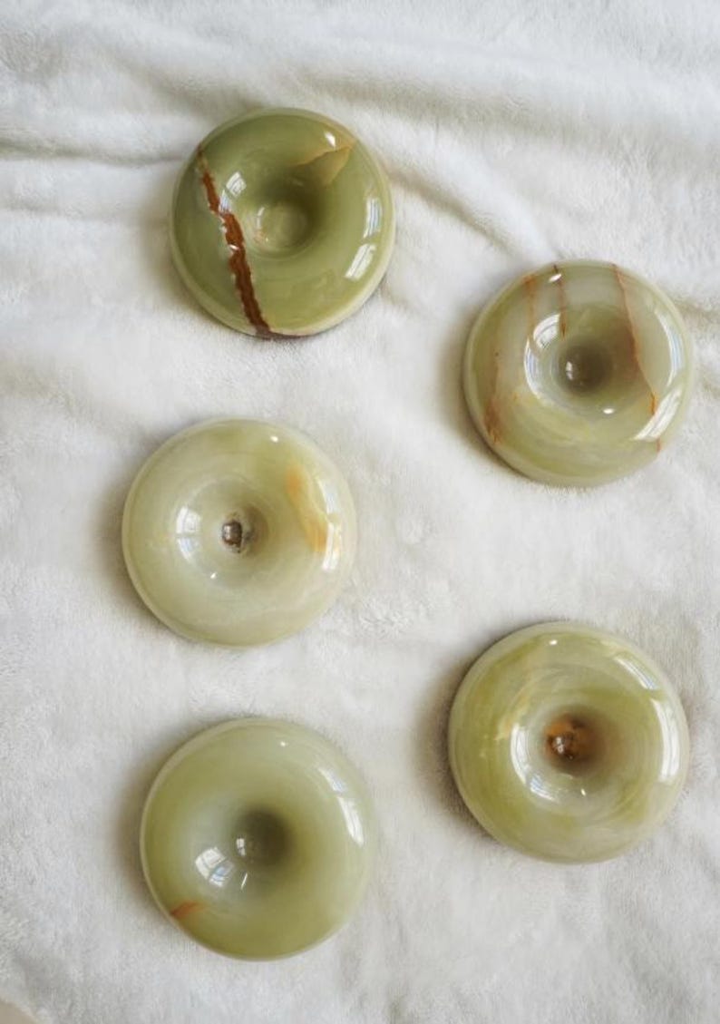 May include: Five circular, donut-shaped stones made of polished green onyx. Each piece features a smooth, glossy surface with natural variations in color, including light green tones and distinct brown mineral veins running through the stone.