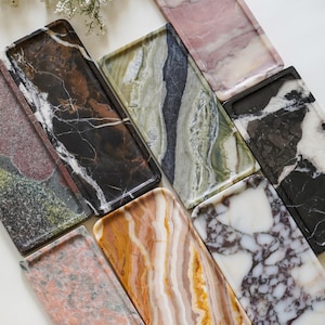 May include: A collection of eight rectangular stone trays featuring various natural patterns and colors, including shades of pink, dark brown, forest green, black, white, and amber, arranged in a scattered layout on a flat surface.
