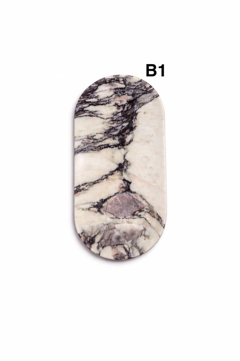 May include: An oval-shaped decorative tray with a marble design. The tray features a white base with dark gray and purple veining. The text "B1" is printed in black at the top of the tray.