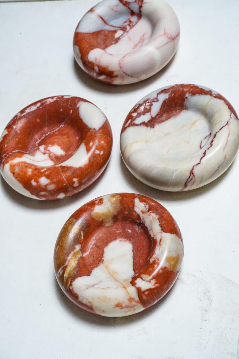 May include: Four circular stone dishes with a polished finish, featuring a marbled pattern of deep red, white, and occasional tan veins. Each dish has a smooth, concave center and a rounded outer edge, displaying natural variations in color and texture.