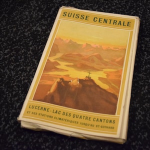 Peut inclure: Une brochure de voyage vintage pour la Suisse centrale, avec une illustration panoramique d'une chaîne de montagnes avec une rivière qui serpente à travers elle. Le texte sur la couverture est "SUISSE CENTRALE LUCERNE-LAC DES QUATRE CANTONS ET SES STATIONS CLIMATÉRIQUES JUSQU'AU ST GOTHARD".