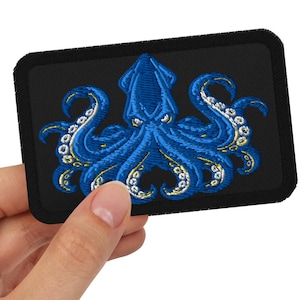 Pode incluir: Um emblema retangular bordado com um design detalhado de lula azul com ventosas brancas nos tentáculos, sobre um fundo preto sólido com uma borda preta espessa, exibindo um trabalho de fio intrincado e cores azuis vibrantes.