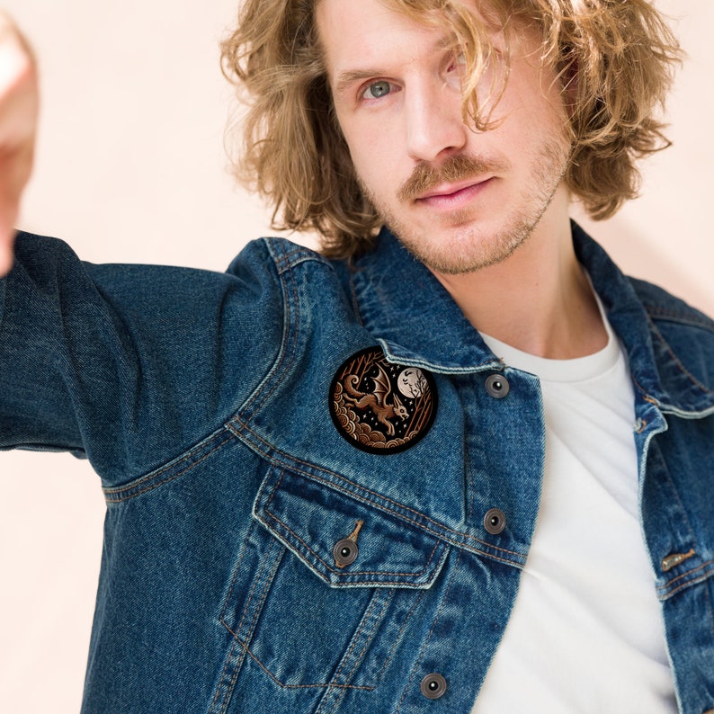 May include: A brown denim jacket with a round embroidered patch featuring a white dragon flying in front of a crescent moon.
