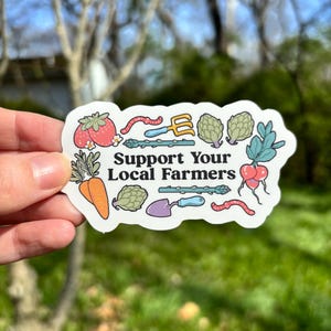 Może przedstawiać: Naklejka z napisem "Support Your Local Farmers" otoczona ilustracjami warzyw i narzędzi ogrodniczych. Naklejka przedstawia pomidora, marchewkę, karczoch, rzodkiewkę i szparagi.