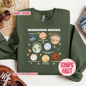 May include: Military green sweatshirt with the text "Neurodiverse Universe" and planet graphics. The design includes phrases like "Choose to Include" and "Celebrate Minds of All Kinds". The sweatshirt also has the text "Ships Fast" on a pink sticker.