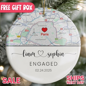 May include: A personalized Christmas ornament with a map of Paris, a red heart, and the word "Paris." It features the names "Liam & Sophia," the word "ENGAGED," and the date 02.24.2025.