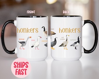 May include: White ceramic mug with a black handle and rim, featuring the word "honkers" in gold lettering. The mug is decorated with illustrations of various goose species. The text "Ships Fast" is on a pink circle.