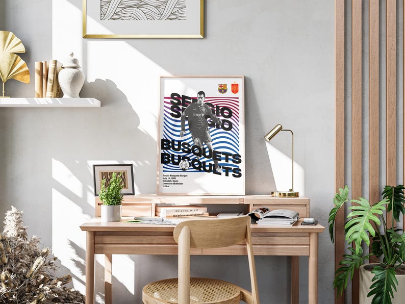 K&ouml;nnte beinhalten: Ein gerahmtes Poster mit einem Schwarzwei&szlig;bild eines Fu&szlig;ballspielers in einem blau-roten Trikot. Das Poster tr&auml;gt den Text "Sergio Busquets" in Schwarzwei&szlig;. Das Poster h&auml;ngt an einer Wand &uuml;ber einem Holztisch mit einer Lampe und einer Pflanze.