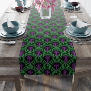 May include: A black table runner with a repeating pattern of green and purple arches. The runner is on a wooden table with two place settings on each side.