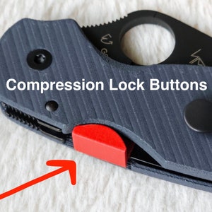 May include: Close-up of a black pocket knife with a red compression lock button. The knife has a textured black handle and a silver pocket clip.