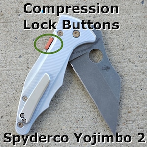 May include: A silver Spyderco Yojimbo 2 folding knife with a black blade. The knife has a compression lock button on the handle.