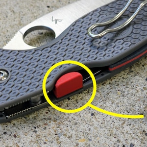 May include: Close-up of a gray pocket knife with a red button. The knife has a textured handle and a silver clip.