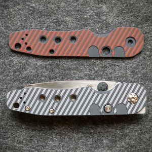 May include: Two pocket knives with different colored handles. The top knife has a red and black striped handle with a silver blade. The bottom knife has a gray and black striped handle with a silver blade.