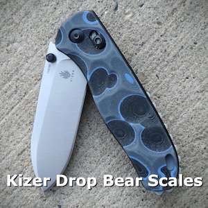 May include: A Kizer Drop Bear pocket knife with blue and black patterned scales. The knife is closed and the blade is visible.