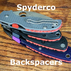 Può includere: Una pila di quattro distanziali Spyderco con bordi in gomma rossa. I distanziali sono di diversi colori: grigio, nero, nero e blu.