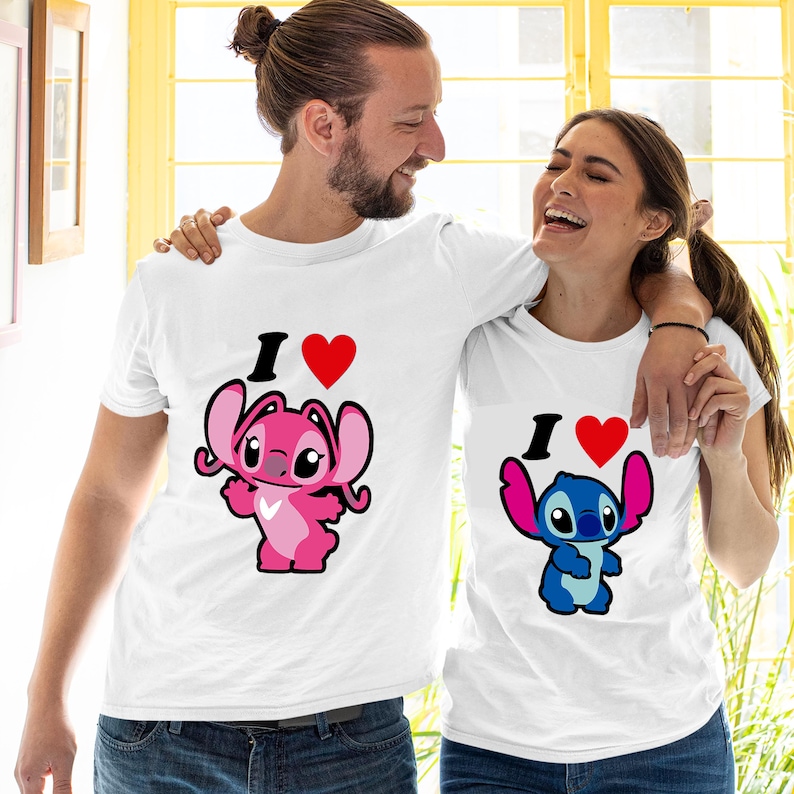 K&ouml;nnte beinhalten: Zwei passende T-Shirts f&uuml;r ein Paar, beide mit wei&szlig;em Hintergrund. Die Shirts zeigen eine rosa und blaue Comicfigur mit dem Text "I love" und einem roten Herzen.