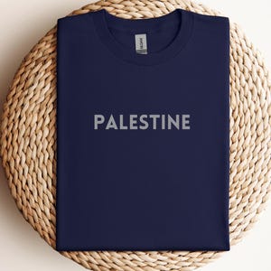 May include: A navy blue t-shirt with the word "PALESTINE" printed in white on the front.