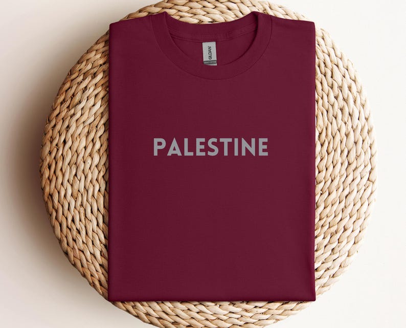 May include: A maroon t-shirt with the word "PALESTINE" printed in grey on the front.