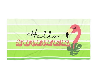 Op de afbeelding: Een groene en witte gestreepte strandhanddoek met de tekst "Hello Summer" in zwart en roze. Een roze flamingo met gesloten ogen en een groen blad bevindt zich aan de rechterkant van de handdoek.