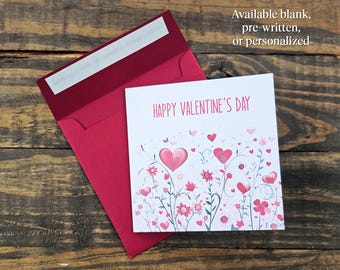 May include: A Valentine's Day card with a pink floral design and the words "HAPPY VALENTINE'S DAY" in pink. The card is inside a red envelope. The text "Available blank, pre-written, or personalized" is also visible.
