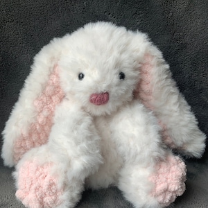 Puede incluir: Un conejito de peluche blanco con orejas y patas rosas. El conejito tiene ojos negros y una nariz rosa.