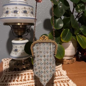 May include: Vintage metal mesh purse with a decorative gold-tone frame and chain handle. The purse features a white, brown, and teal geometric pattern with fringe at the bottom. A classic accessory.