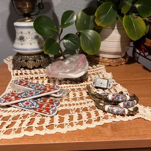 Könnte beinhalten: Eine Sammlung von Vintage-Keramik-Schubladengriffen und dekorativen Elementen. Die Schubladengriffe weisen ein rot-weiß-blaues Blumenmuster mit Messingbeschlägen auf. Passende Keramik-Schranktürgriffe und eine dekorative Lampe sind ebenfalls zu sehen.