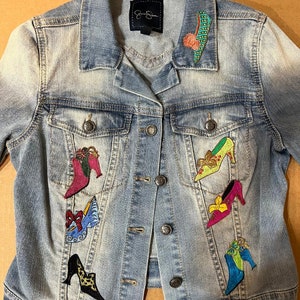 May include: A light blue denim jacket with embroidered shoe designs. The shoes are in various colors and styles, including red, green, blue, and yellow.