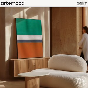 May include: Abstract art print with green, white, blue, and orange stripes in a black frame hanging on a wall above a wooden cabinet. The cabinet is next to a white, fluffy, oval-shaped chair.