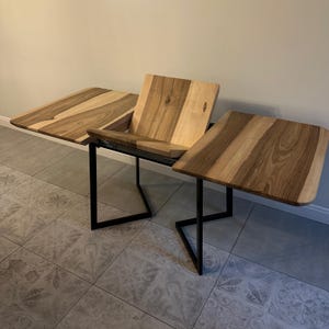 K&ouml;nnte beinhalten: Holztisch mit einzigartigem Design. Die Tischplatte besteht aus hellen und dunklen Holzpaneelen. Der Tisch hat ein schwarzes Metallgestell und ist im geschlossenen Zustand ca. 76 cm lang und im ge&ouml;ffneten Zustand 152 cm lang.