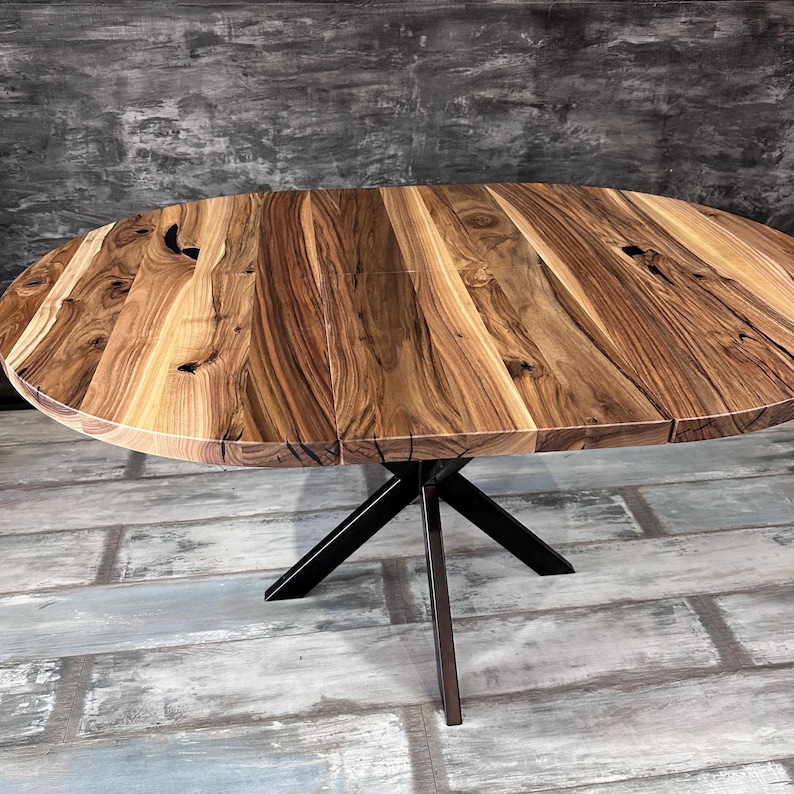 May include: A round dining table featuring a natural wood grain tabletop with visible knots and dark brown streaks. The table is supported by a black metal base with four angled legs that meet at a central point beneath the circular surface.
