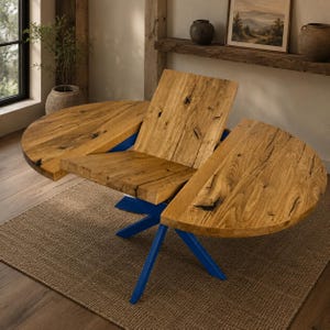 Op de afbeelding: Een eettafel met een natuurlijk houten blad met zichtbare nerven en donkere knoesten, bestaande uit drie afzonderlijke delen. De tafel wordt ondersteund door een felblauw metalen onderstel met schuine poten die vanuit een centraal punt uitlopen.