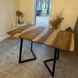 May include: A wooden dining table with a light and dark brown striped pattern. The table has a rectangular top with rounded corners and is supported by black metal legs. The table is approximately 60 inches long and 30 inches wide.