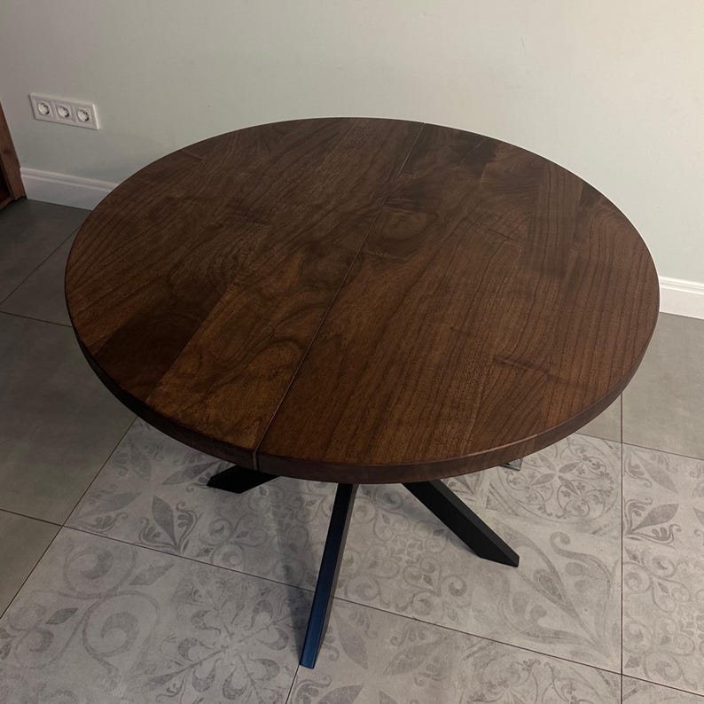 Peut inclure: Une table ronde en bois avec une finition brun fonc&eacute;. Le plateau est soutenu par un pi&egrave;tement en m&eacute;tal noir. La table mesure environ 100 cm de diam&egrave;tre.