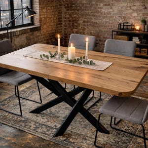 May include: A rectangular wooden dining table with a light brown finish, supported by black metal legs. The table is set with candles and greenery. Gray upholstered chairs surround the table, and a patterned rug is beneath.
