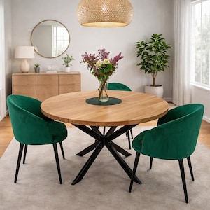 May include: A round wooden dining table with a black metal base, surrounded by four green velvet chairs. A vase of flowers sits on the table, which is set on a light-colored rug. A woven light fixture hangs above the table.
