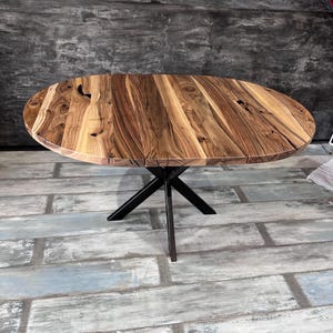 May include: A round dining table featuring a natural wood grain tabletop with visible knots and dark brown streaks. The table is supported by a black metal base consisting of four intersecting legs that meet at a central point beneath the surface.